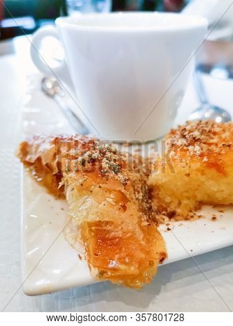 Delicious Greek sweet pastry named Galaktoboureko, made of semolina custard in filo, served with honey in white plate.