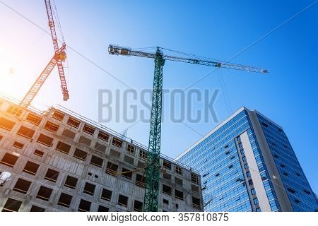Bottom View Of A Building Under Construction With High Construction Cranes And A Glass Tower In The 