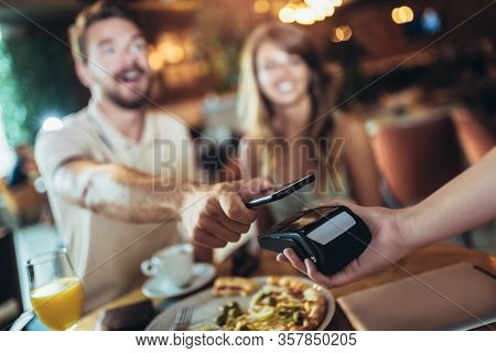Happy Couple Using Mobile Phone And Making Contactless Payment In A Restaurant. S