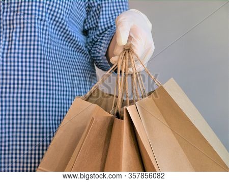 Courier In A Checkered Blue Shirt With Medical Latex Gloves Safely Delivers Online Purchases In Brow