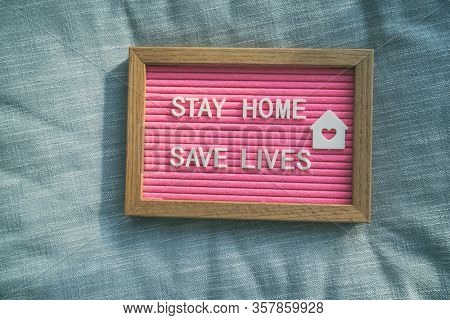 Coronavirus quote stay home, save lives pink felt board sign with message of self isolation for social responsability on home sofa background. COVID-19 text to promote staying at home.