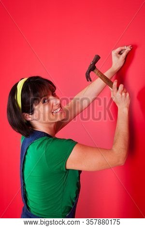 woman driving a nail in a red wall