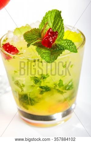 Icy lemonade with mint leaves. Glass of cold beverage with marmalade and crushed ice. Refreshing drink with colorful gummy bears closeup view. Minty sweetened water on white background