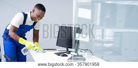 Young Male Maid Cleaning Glass Desk With Feather Duster In Office