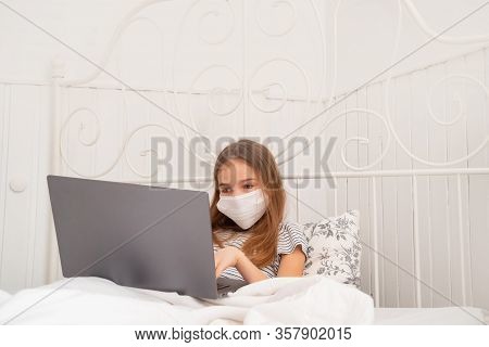 Sick Teenage Girl In A Medical Mask Lying In Bed And Studying On Laptop. Distance Learning.