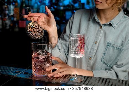 Young Woman Barman Holds In Her Hand Strainer Over Large Glass With Pink Drink
