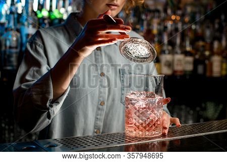 Close-up Young Womans Hand Holds Strainer Over Large Glass With Pink Drink