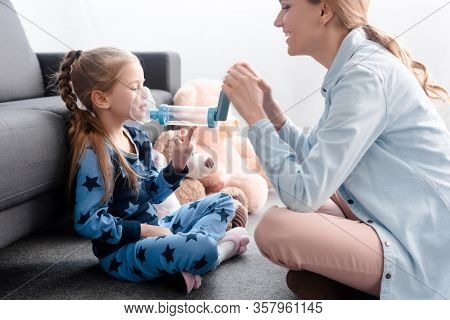 Happy Mother Holding Inhaler With Spacer Near Sick Kid