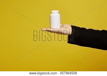 A White Bottle Of Drugs On A Male Palm On Yellow Background, Isolated With Copy Space. Healthcare Co