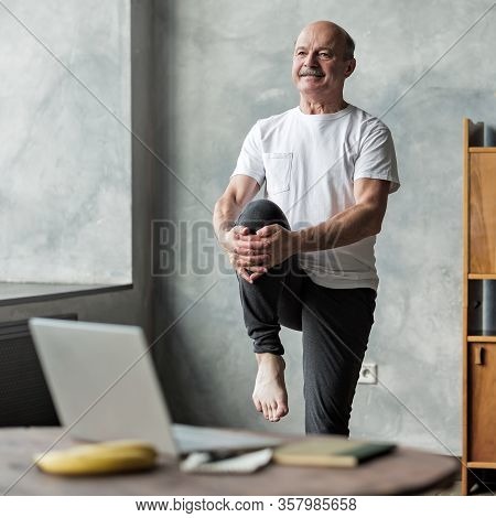 Man Doing Yoga Exercise At Home Using Online Lesson On Notebook.