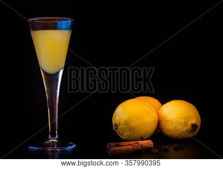 Limoncello In Elegant Liquor Glass With Lemon, Cinnamon And Cloves On Dark Background. Sicilian Lemo