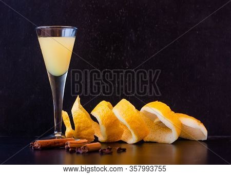 Limoncello In Elegant Liquor Glass With Lemon Zest, Cinnamon And Cloves On Dark Background. Sicilian