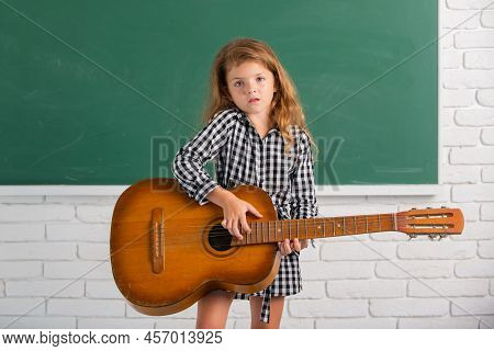 Kid Girl On Musik Lesson At School. Elementary School Child Hold Guitar In Class.