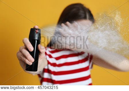 Young Woman Covering Eyes With Hand And Using Pepper Spray On Yellow Background