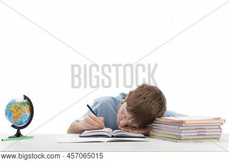 Primare Schoolboy With Glasses Is Tired While Doing Homework. Boy Sleeps At His Desk Portrait Of Tir