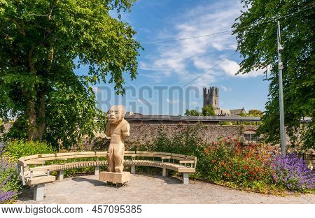 Limerick, Ireland - June 4, 2022: Beautiful Wooden Statue And The Bench Near River Shannon With St M