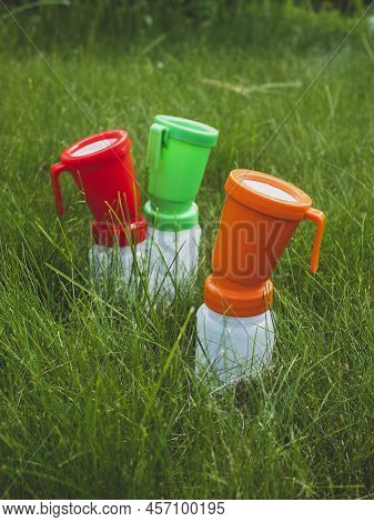 Three Colored Teat Dip Cups For Cattle On The Grass, Selective Focus. Concept Of Hygiene And Disinfe