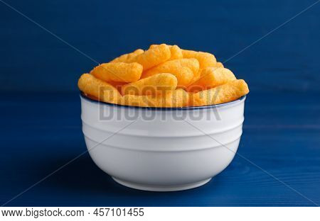 Bowl Of Tasty Cheesy Corn Puffs On Blue Wooden Table