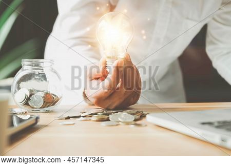 Businessman Holding Lightbulb On Coins Stacking On Desk With Note For Planning Money Finance.saving 