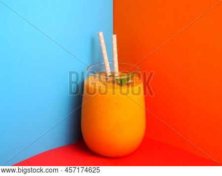 Glass Glass With A Bright Orange Smoothie On An Abstract Colored Background.