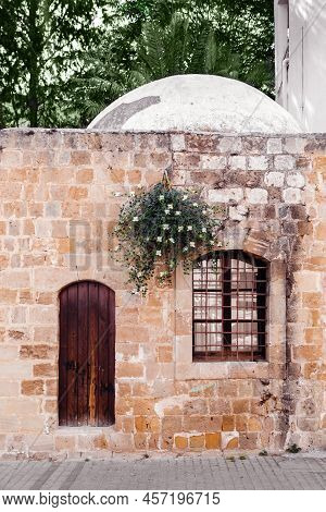 Old Building With Door, Window And Flowering Caper Bush On Stone Wall Background.