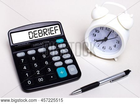 On The Light Table There Is A Black Calculator With The Text Debrief On The Scoreboard, A Pen And A 