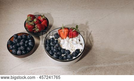 Curd With Fresh Blueberries And Strawberries In A Plate And Bowls With Fruits On A Light Background.