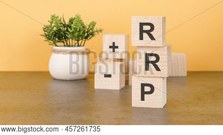 Rrp The Word On Wooden Cubes, Cubes Stand On A Reflective Surface, In The Background Is A Business D