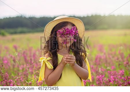 A Beautiful Playful Little Girl In A Straw Hat, Holds A Bouquet Of Burgundy Viscaria Flowers
