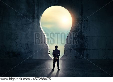 Businessman Looking Out Of Abstract Opening In Wall With Bright Daylight In Concrete Interior. Conce