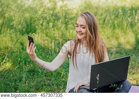 Girl Sits Outdoors And Works At A Laptop. Makes A Video Call On The Phone. Freelance. Selfeducation.