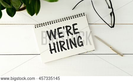 We're Hiring Words Written On A White Sheet And A Wooden Background. Concept In Business.