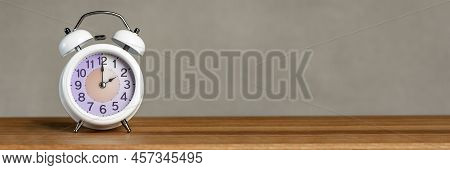 Two Hours On The Alarm. A White Alarm Clock Stands On A Wooden Table. The Clock Hand Points To 2 Ocl