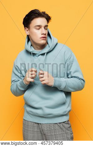 A Handsome Teenager Stands On An Orange Background In A Light Hoodie And Pulls Aside The Lacing