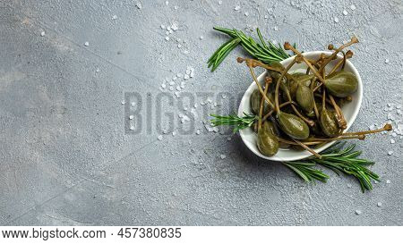Capers. Marinated Or Pickled Canned Capers Fruit With Fresh Rosemary In A Small Bowl, On Gray Backgr