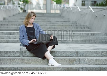 Portrait Of A Concentrated Young Businesswoman Working At Her Laptop. Bottle Of Water Near The Busy 