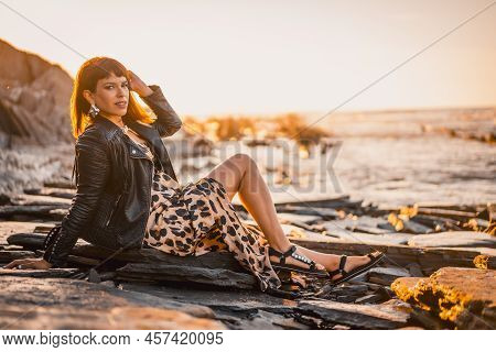 Summer Street Style On A Beach Next To Rocks Of A Young Brunette Caucasian Woman In A Leopard Dress 