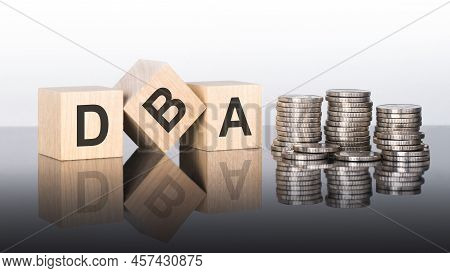Dba - Text Is Made Up Of Letters On Wooden Cubes Lying On A Mirror Surface, Gray Background. Stacks 