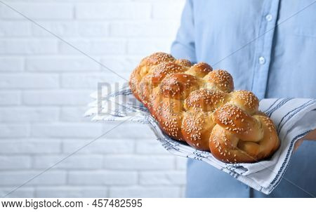 Closeup View Of Woman Holding Homemade Braided Bread Near White Brick Wall, Space For Text. Traditio