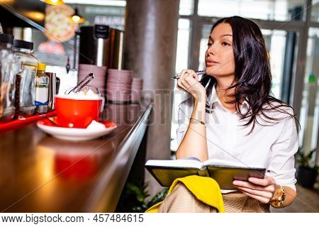 Indian Reading Notes In Notepad While Sitting Near Table Bar And Drinling Cup Of Tea