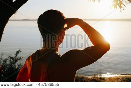 Back View Of Unrecognizable Athletic Man Enjoying Beautiful Sunset At Lake. Inspirational Guy Lookin