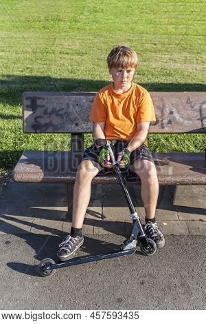 Eschborn, Germany - August 23, 2009: Exhausted Boy Sitting On A Bench With His Scooter.