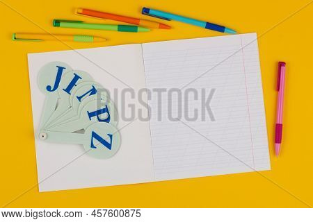 School Notebook On A Yellow Background With Copy Space For Text, Colorful Pens, English Alphabet. Ba
