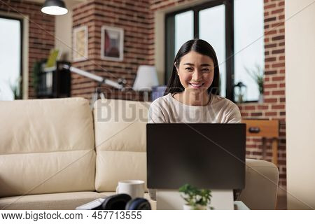 Portrait Of Smiling Neautiful Asian Woman Looking Straight To Camera In Modern Flat Living Room. Tec