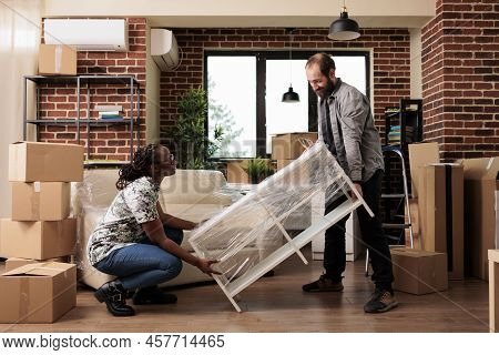 Diverse Couple Decorating New Rented Apartment To Move In And Enjoy Relocation Together, Settling In