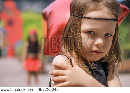 The Little Sisters Quarreled Over A Trifle. The Hippie Girl Stands With Her Hands Folded Busily With