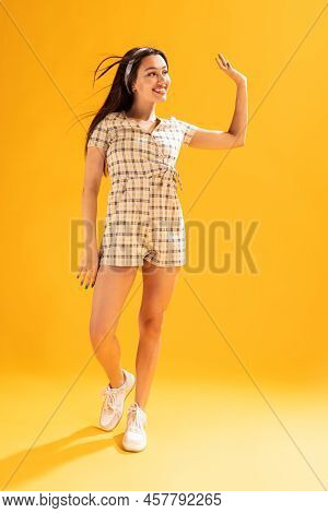Portrait Of Beautiful Young Girl In Stylish Summer Outfit Posing, Waving Isolated Over Yellow Studio