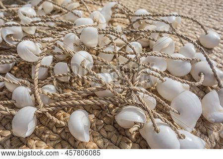 White Shells Strung Like Beads On A Rope Lie On A Mat On The Beach. Beach Decor On A Warm Sunny Day 