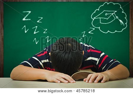亚洲男孩睡在一本书上和毕业后的梦想