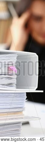 Close-up Of Tired And Exhausted Woman Looks At Documents Touch Head With Hands. Huge Pile Of Documen